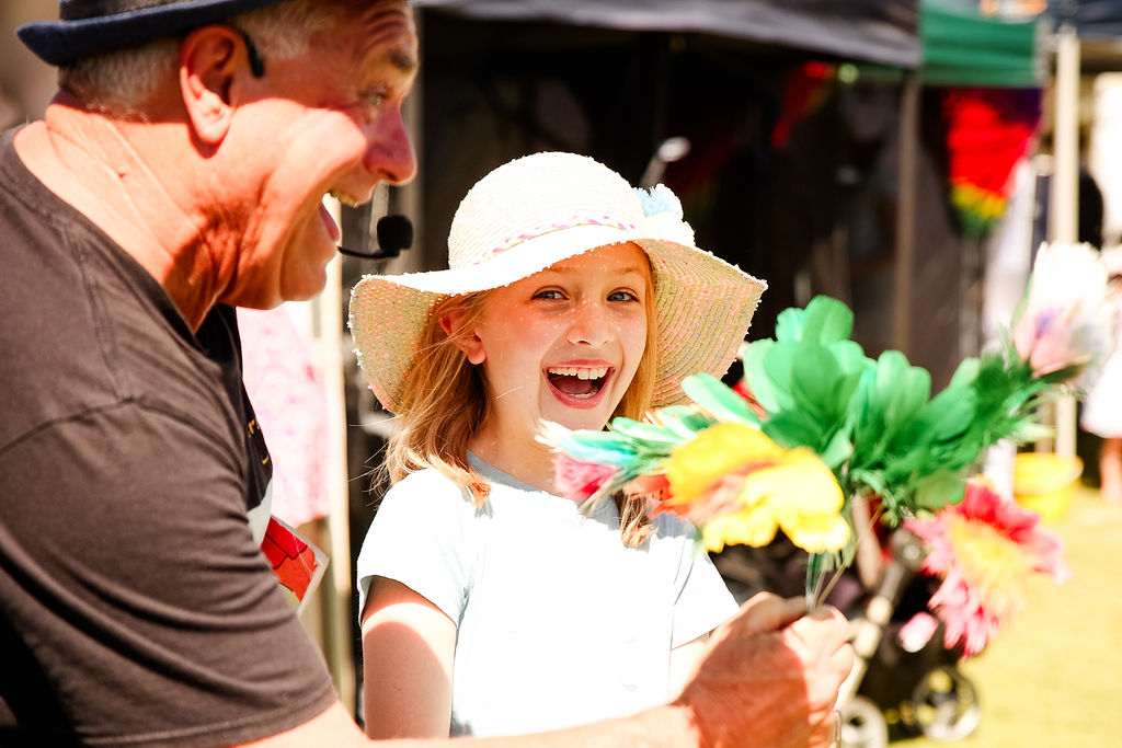 Girl delightedly smiling as she is presented by a bouquet of paper flowers by a magician.